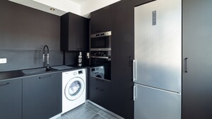 Una cocina moderna con un refrigerador de acero inoxidable, horno empotrado, lavadora y muebles de cocina oscuros.