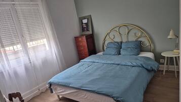 Ein Schlafzimmer mit Bett, Kommode, Nachttisch und einem Fenster mit Vorhängen.