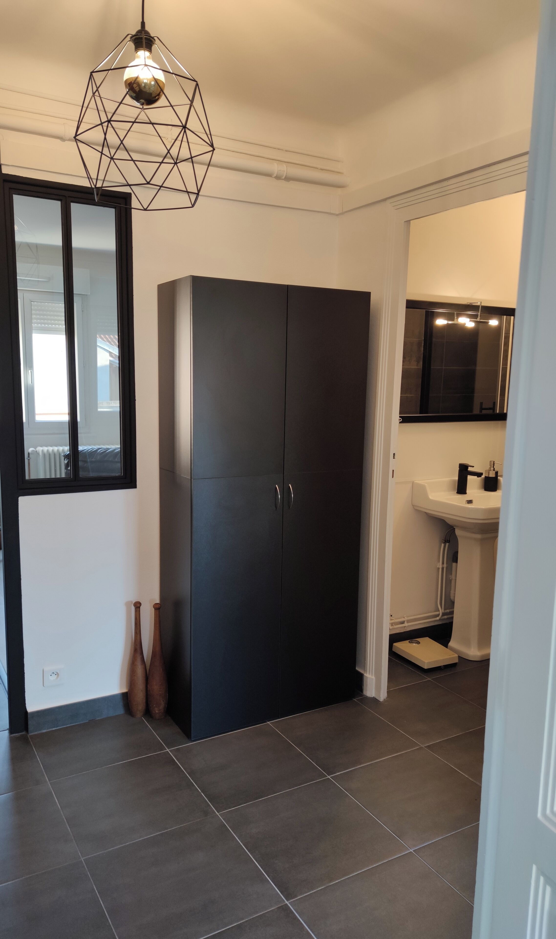Une salle de bain moderne avec un meuble sombre, un lavabo blanc et un luminaire aux formes géométriques.