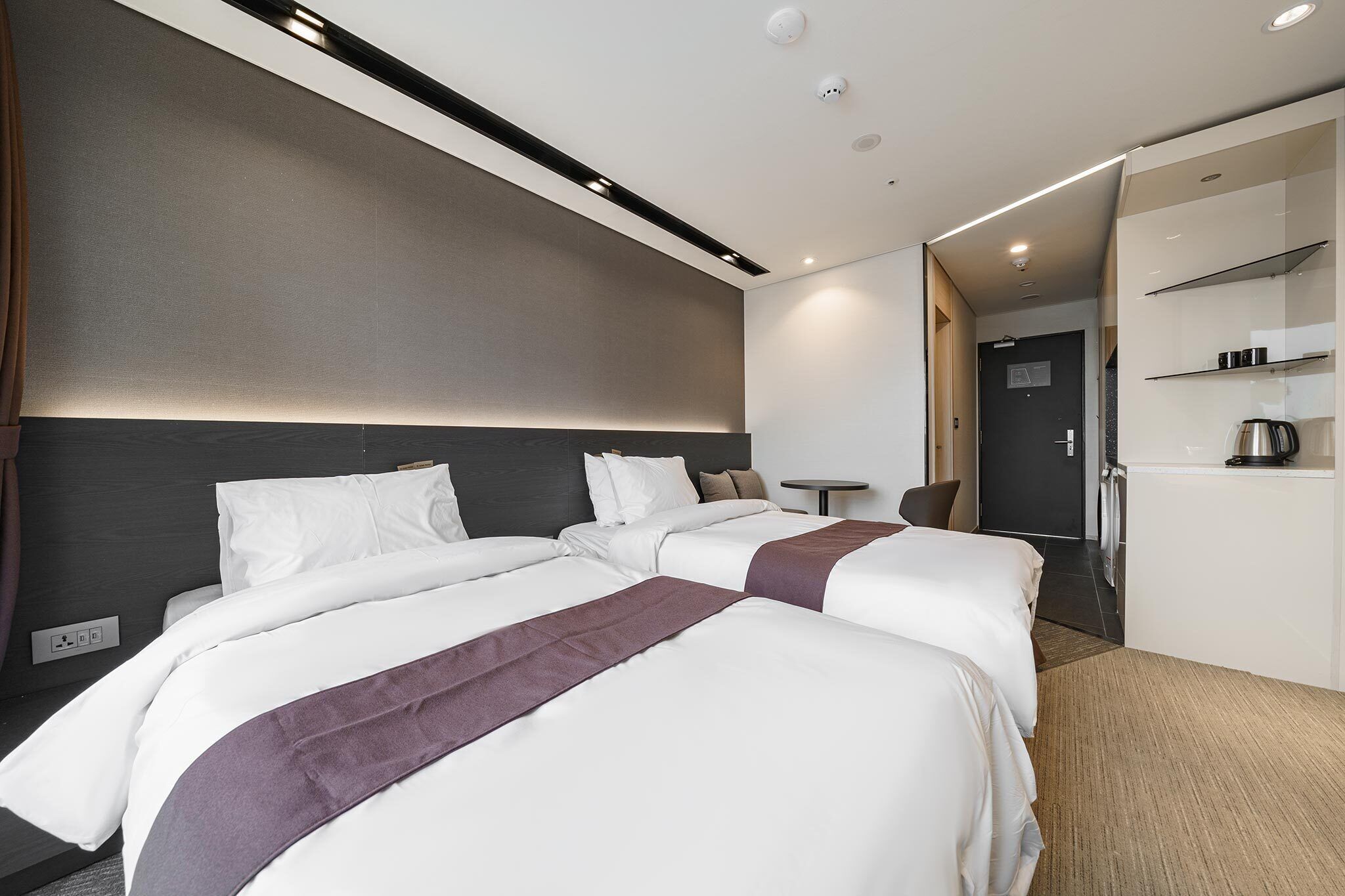 Una habitación de hotel moderna con dos camas, un escritorio pequeño y una kitchenette.