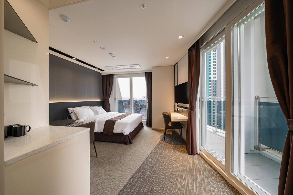 A hotel room with a bed, desk, and large window.