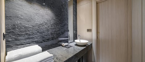 Un baño moderno con encimera de mármol negro, un lavabo blanco y un espejo grande.