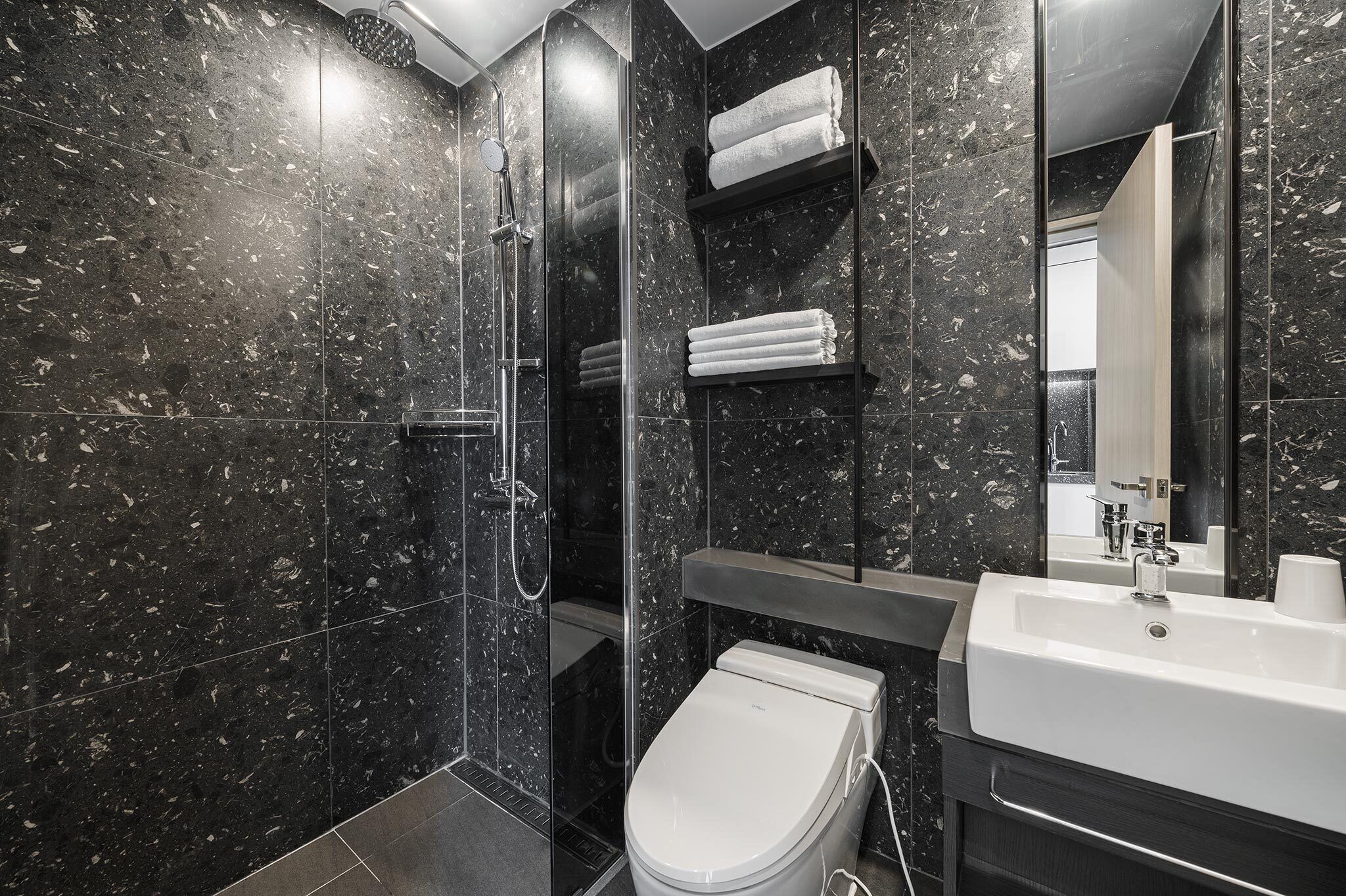 Un bagno moderno con doccia vetrata, un water bianco e un grande specchio sopra un lavandino bianco.