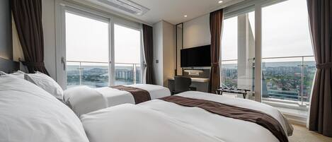 A hotel room with two beds, a desk, a chair, a TV, and large windows offering a city view.
