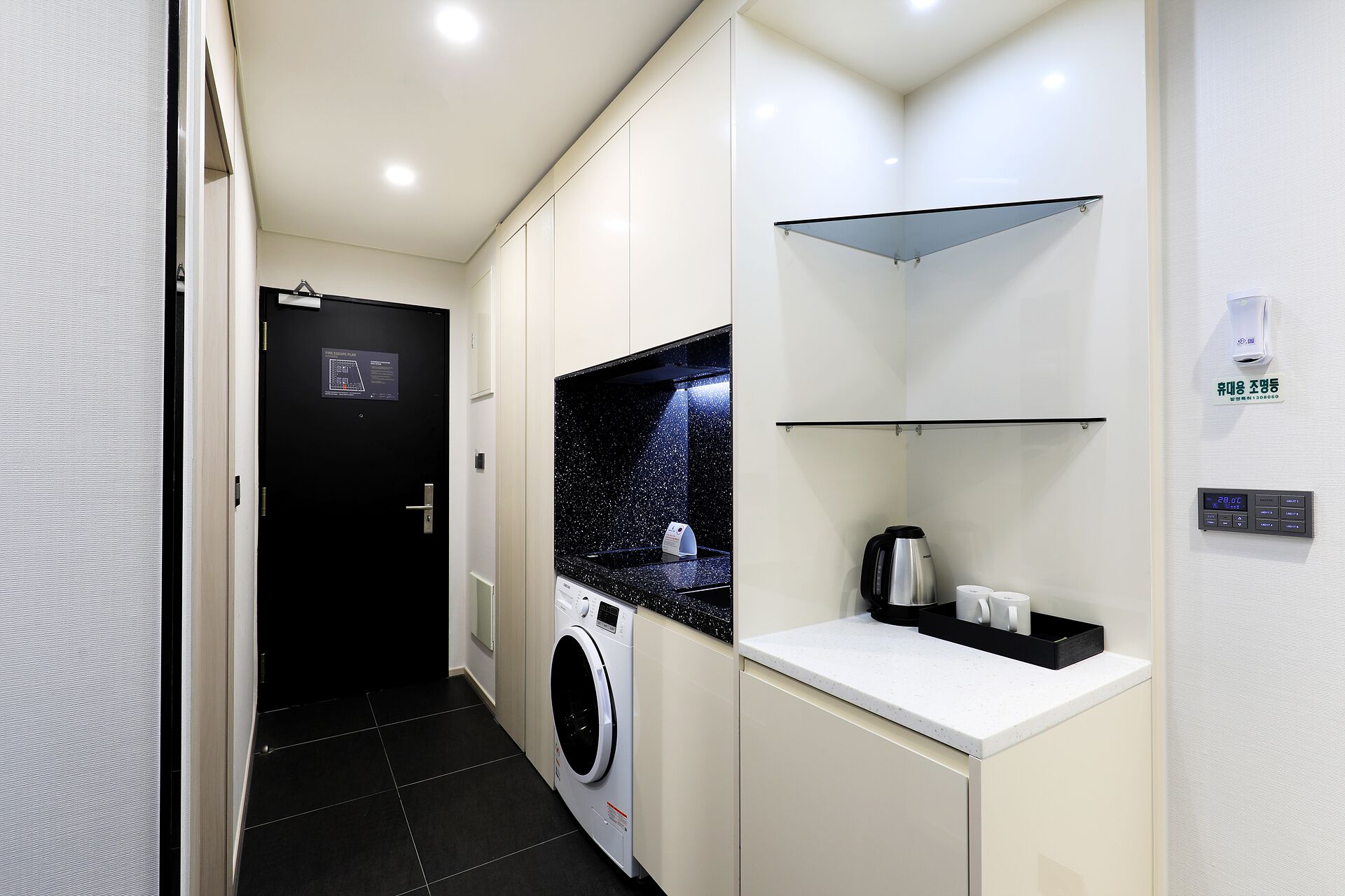 Habitación de hotel compacta con lavadora, cafetera y una pequeña encimera.