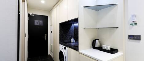 Habitación de hotel compacta con lavadora, cafetera y una pequeña encimera.