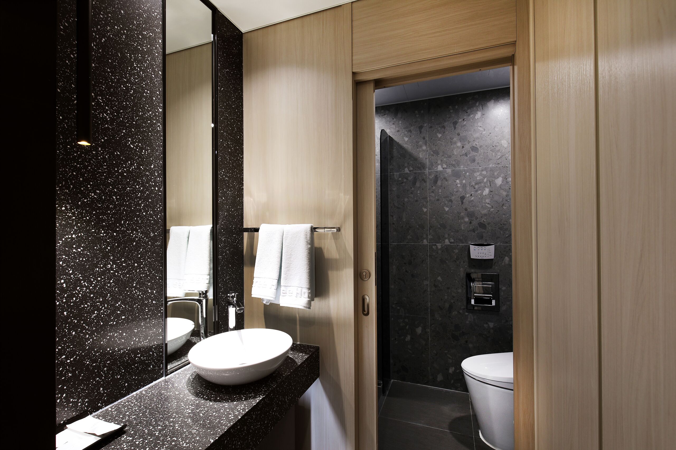 A modern bathroom with a large mirror, a round sink, a toilet, and a shower area.