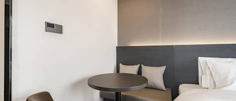 A modern hotel room with a bed, a small round table, a sofa, and a chair.