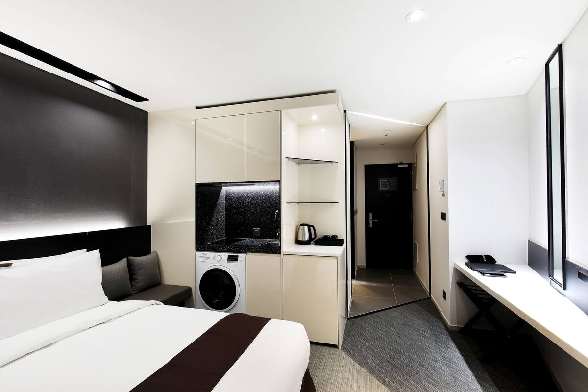 A modern hotel room with a bed, a washing machine, a desk, and a television.