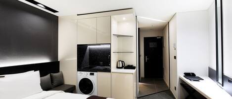 A modern hotel room with a bed, a washing machine, a desk, and a television.