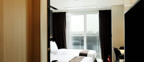 Una habitación de hotel con dos camas, un ventanal grande, un escritorio y un televisor.