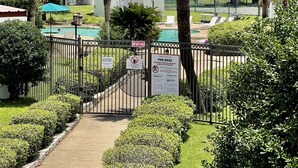 A gated pool area with palm trees, a tennis court, and a building with balconies.