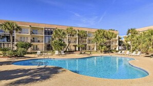 A hotel with a swimming pool, palm trees, and a clear blue sky.