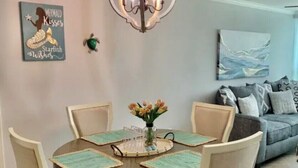 A dining area with a round table, four chairs, a chandelier, a wall-mounted artwork, and a sofa in the background.