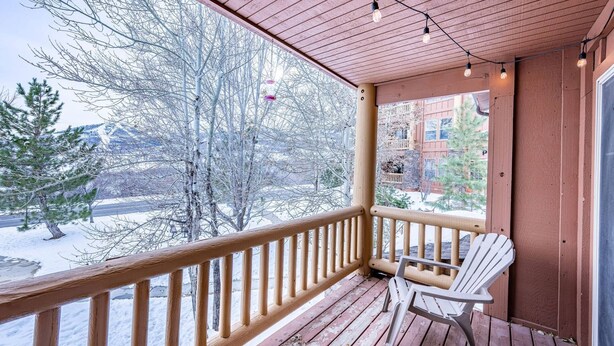 Une terrasse en bois avec une chaise blanche, une rambarde et une vue sur des arbres et des bâtiments recouverts de neige.
