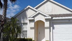 A single-story house with a white exterior, a garage door, and a small front porch. - Hampton Lakes Homes (Davenport)
