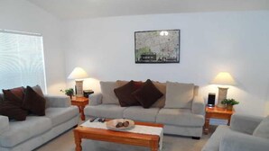 A living room with a sofa, two side tables, a coffee table, and a painting on the wall. - Hampton Lakes Homes (Davenport)