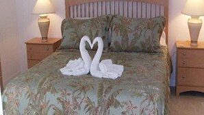 A bed with a floral bedspread and two white towels arranged in the shape of swans. - Hampton Lakes Homes (Davenport)