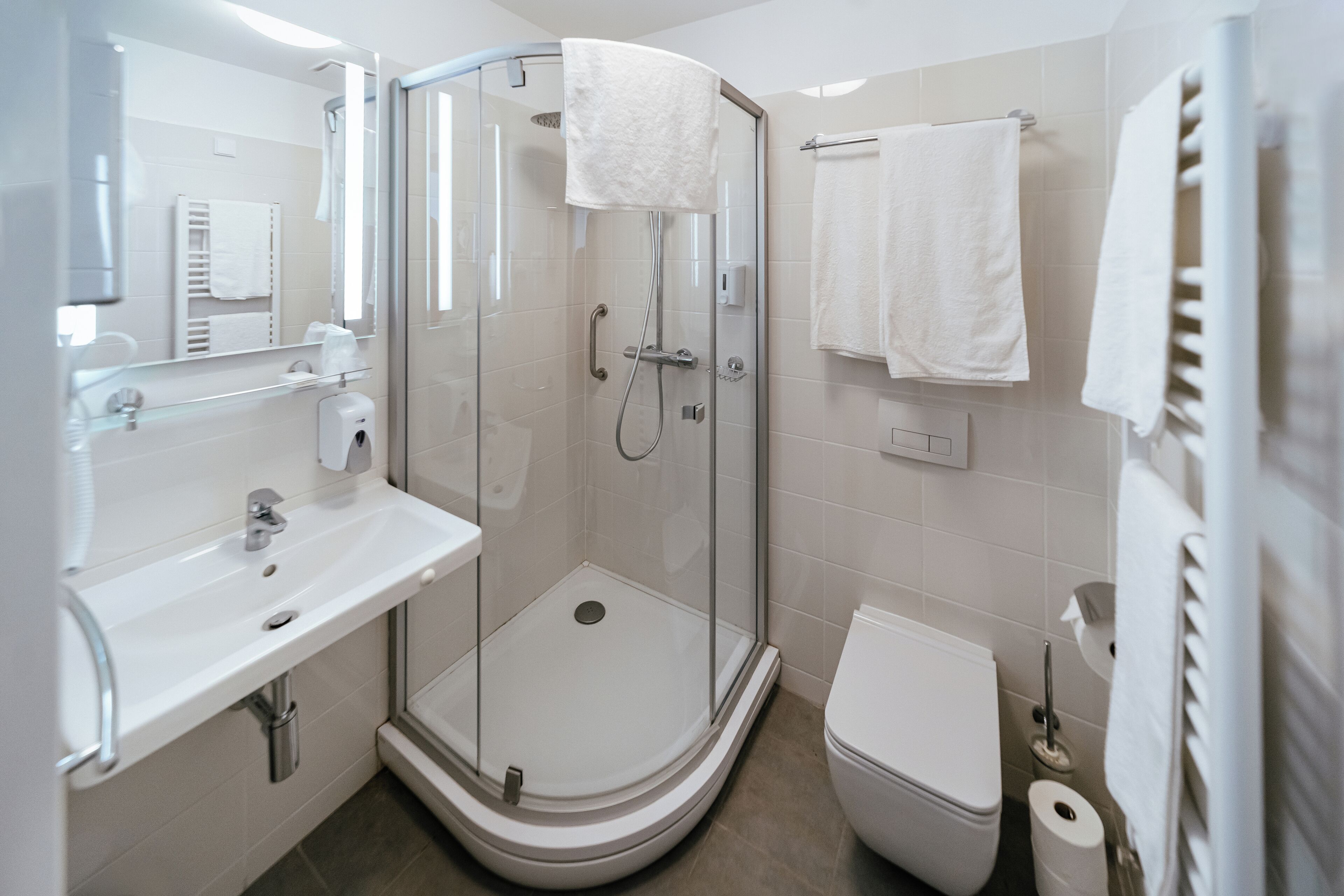 Un baño moderno con ducha de vidrio, lavamanos blanco y retrete.