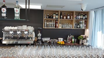 Una zona de bar con una máquina de café, estantes llenos de botellas de licor y una gran cantidad de copas de vino.