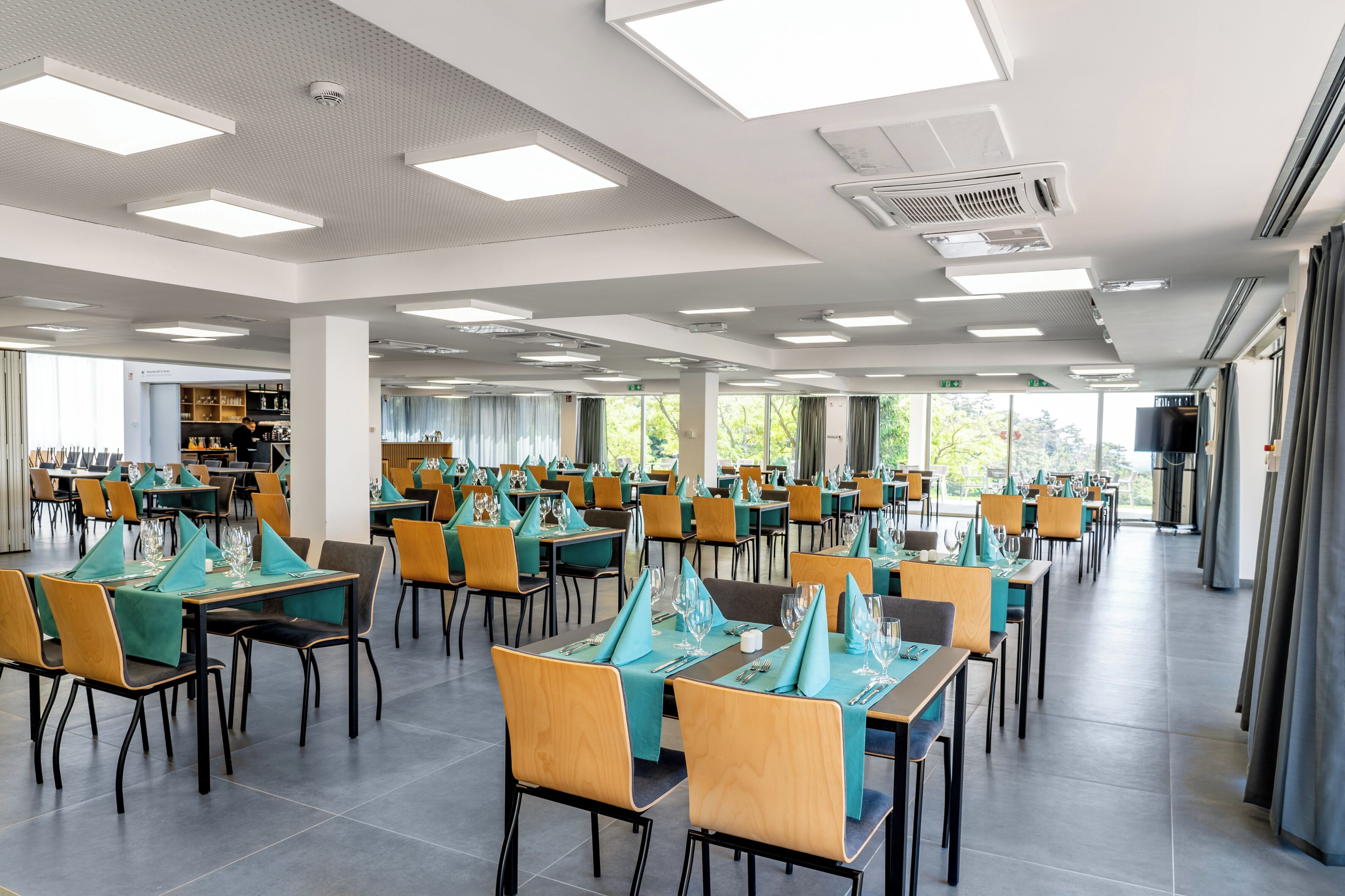 Un vaste espace dédié à la salle à manger, avec de nombreuses tables et chaises, de grandes fenêtres et un design de plafond moderne.