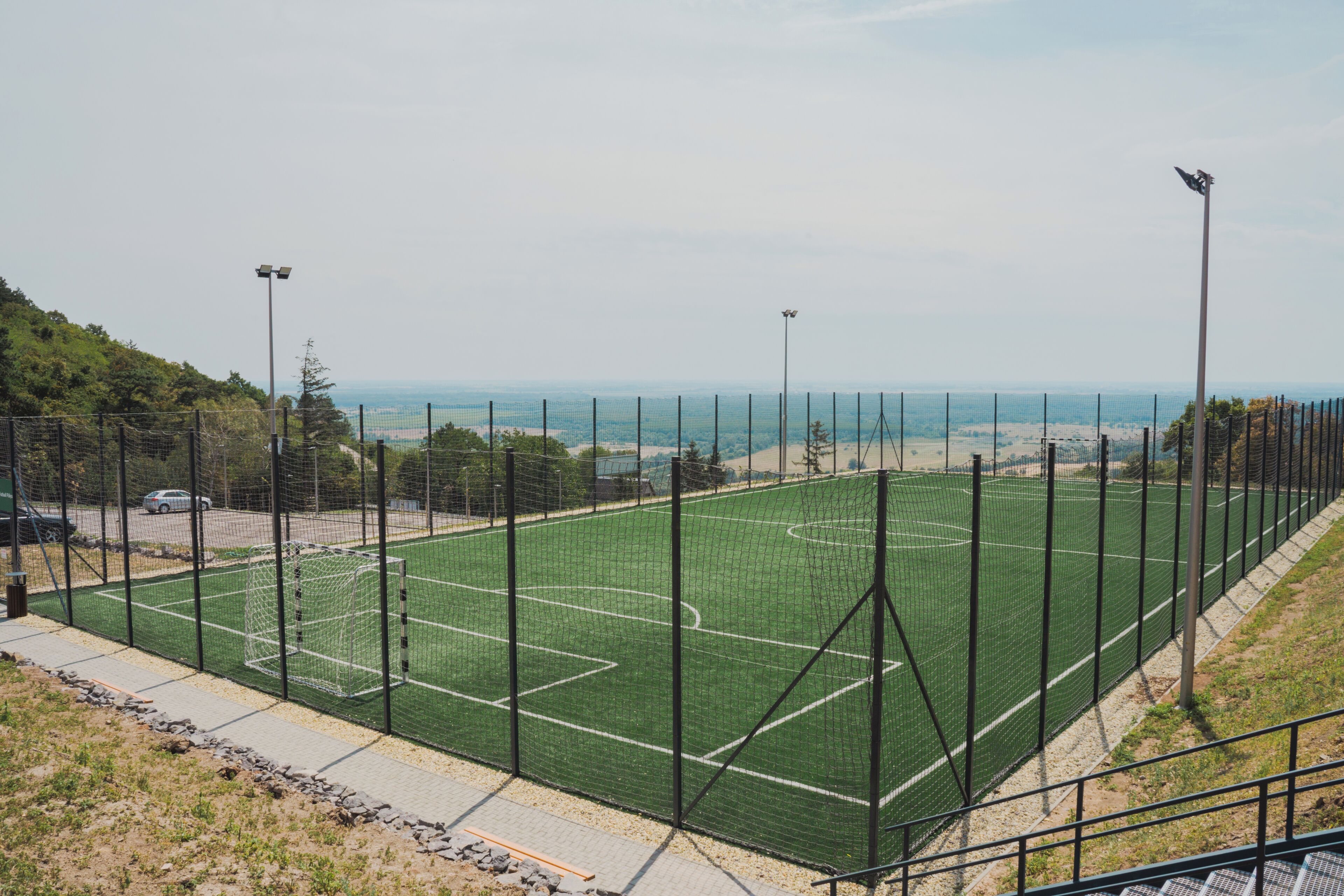 Un campo deportivo con porterías, rodeado de una valla y con iluminación artificial.