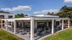 Eine Außenpatio mit mehreren Tischen und Stühlen, einer überdachten Sitzgelegenheit und einem modernen Gebäude im Hintergrund.