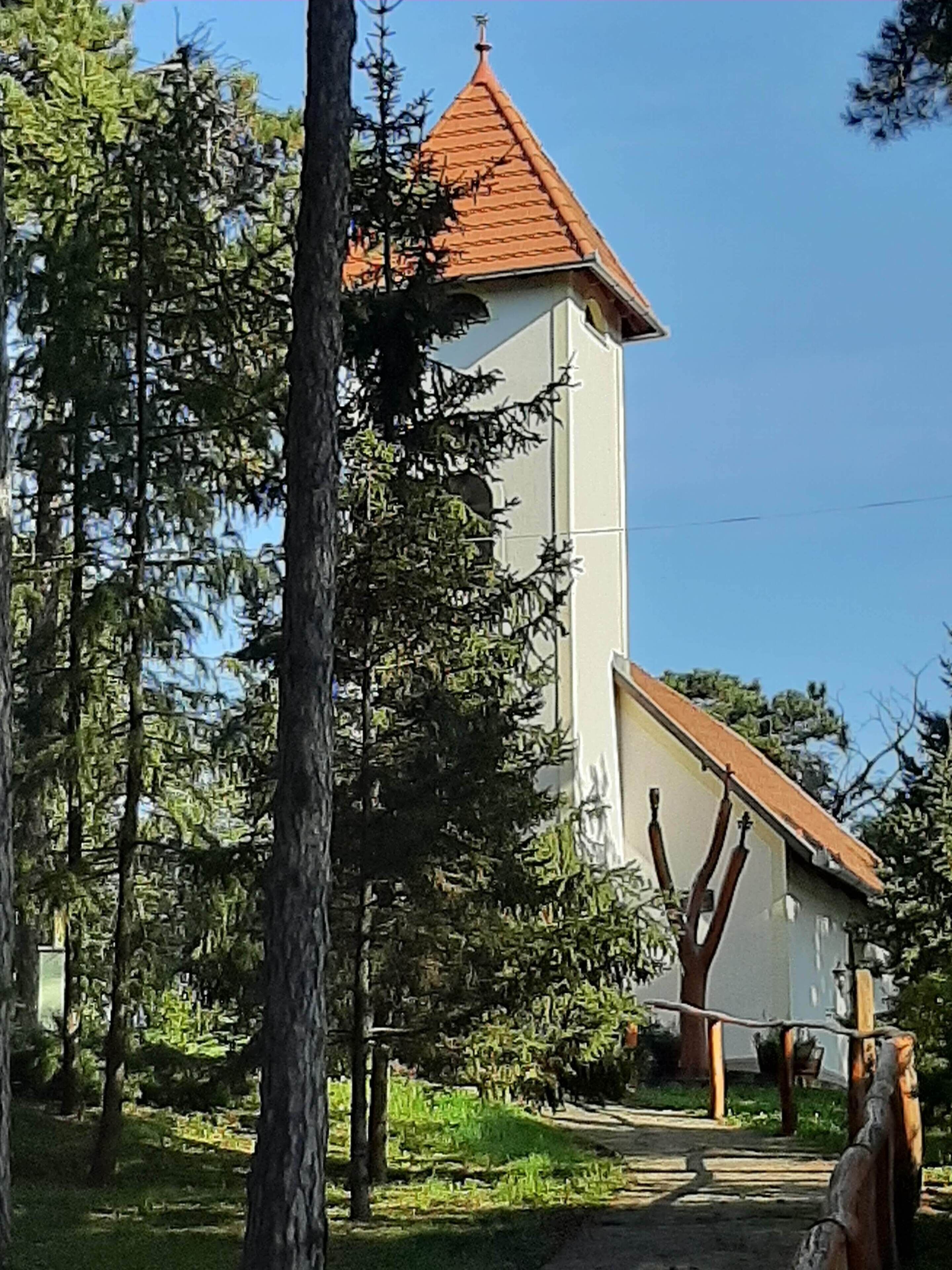 Una iglesia de techo rojo y paredes blancas, rodeada de árboles.