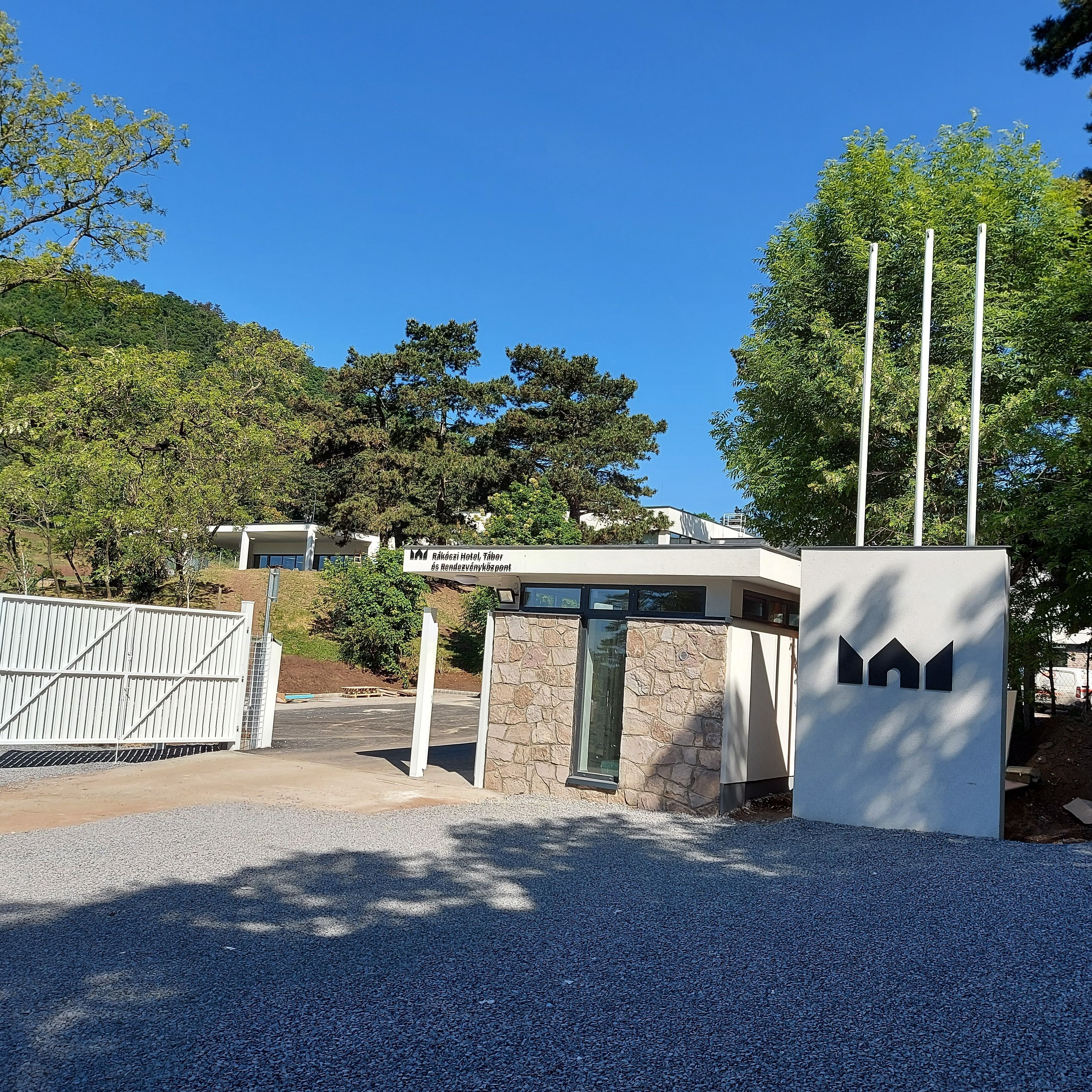 Un edificio moderno con fachada de piedra, entrada protegida por una reja y un cartel que indica que es el Hotel Rákodai, Tábér.