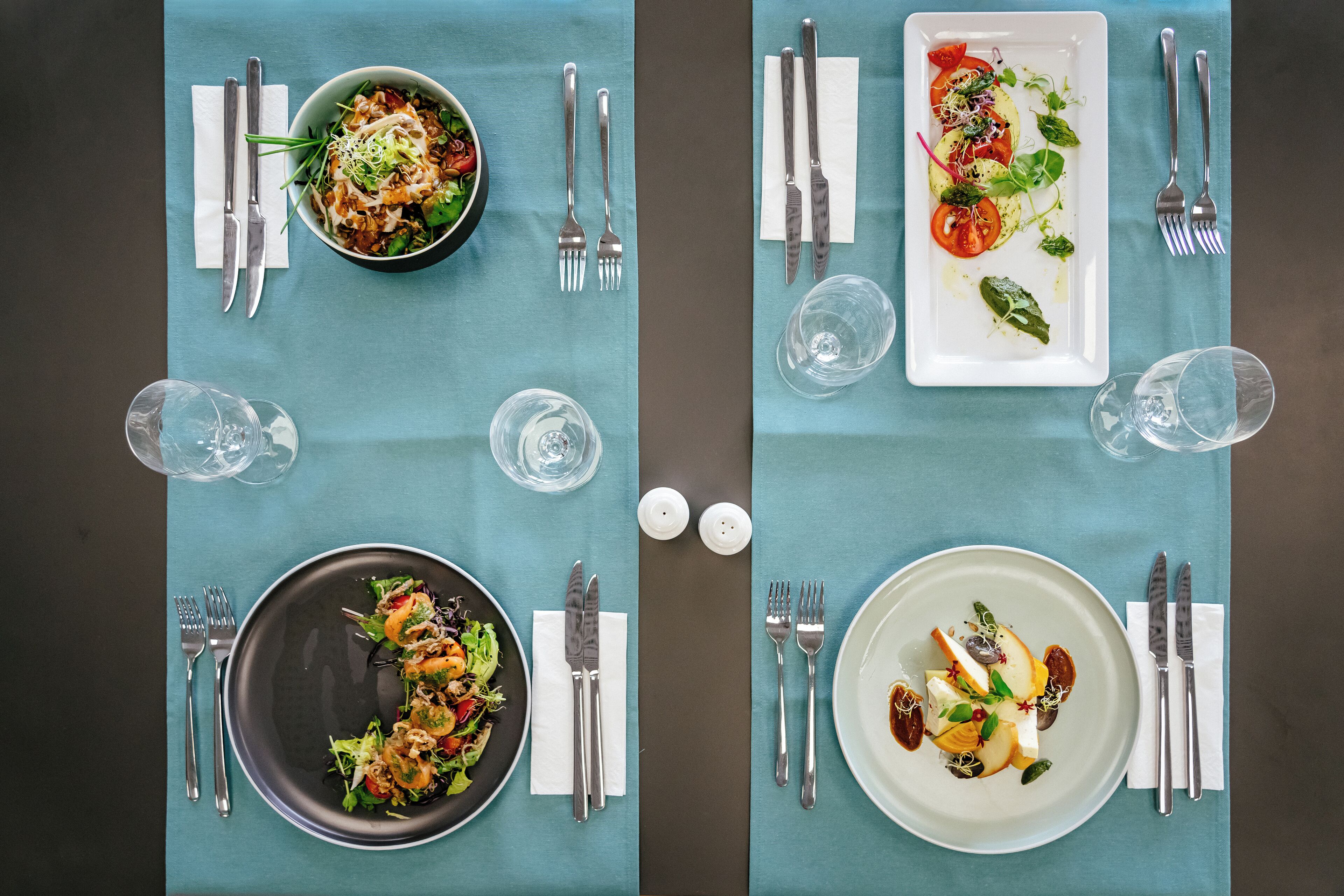 Una mesa de comedor dispuesta con dos platos de comida, cubiertos y vasos.