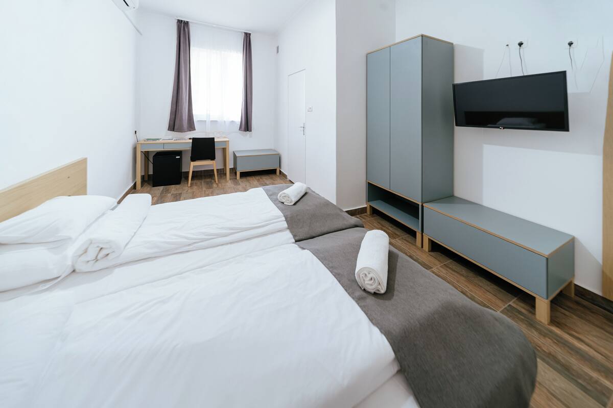 A hotel room with two beds, a desk, a chair, a TV, and a wardrobe.