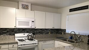 A modern kitchen with white cabinets, a granite countertop, a stove, a microwave, and a sink. - A Beautiful Colorado River Retreat (Bullhead City)