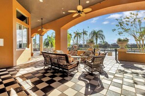 Relax in a serene outdoor space with wicker chairs and a small table, surrounded by a low wall and large windows offering a view of palm trees.
