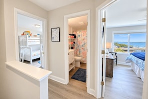 A bedroom with a view of the sea, a bathroom with a shower curtain, and a child's room with a bunk bed.