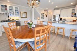 A modern kitchen with white cabinets, a central island, and a dining area with wooden chairs and a round table. - Experience the island lifestyle, live like a local! 4Br/3.5ba waterfront duplex. (Wrightsville Beach)