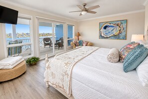 Un dormitorio con una cama grande, un ventilador de techo y vistas a un balcón con mobiliario exterior.
