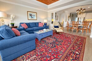A living room with a blue sofa set, a coffee table, a patterned rug, and a dining area with wooden chairs and a chandelier. - Experience the island lifestyle, live like a local! 4Br/3.5ba waterfront duplex. (Wrightsville Beach)
