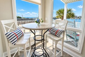Un balcon avec une table ronde et deux chaises, chacune agrémentée de coussins à rayures, donnant sur une marina où sont amarrés des bateaux et sur un pont.