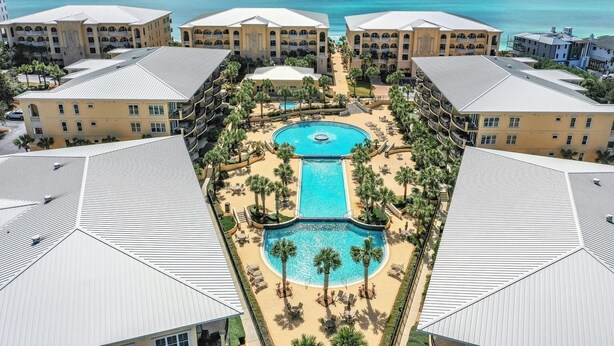 A resort with a central pool, multiple buildings, and a view of the ocean.