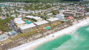 An aerial view of a coastal resort with multiple hotel buildings, a beach, and clear turquoise waters.