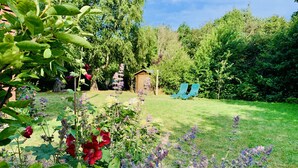 Un jardín con una pequeña estructura de madera, dos sillas de jardín azules y una variedad de plantas florecientes.