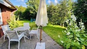 Un patio con mesa y sillas, una sombrilla y un jardín con flores y follaje.