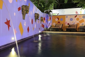 A swimming pool with a colorful mural, lounge chairs, and a tiled floor.
