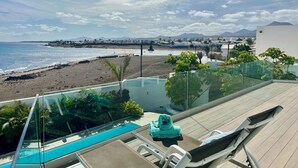 A poolside area with a glass barrier, lounge chairs, and a view of the beach and ocean. - Villa del Mar - Beachhouse (Playa Honda)