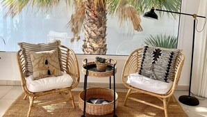 A room with two wicker chairs, a small table with a plant, and a large window with a view of palm trees. - Villa del Mar - Beachhouse (Playa Honda)