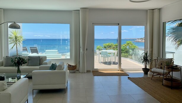 A modern living room with a large sliding glass door leading to a balcony with a view of the sea. - Villa del Mar - Beachhouse (Playa Honda)