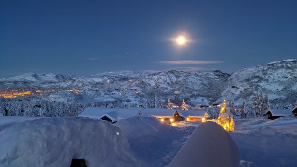 A snowy mountain landscape at night with illuminated buildings and a visible moon. - Fantastic and large cottage on top of Furuåsen in the heart of Sirdal (Tjørhom)
