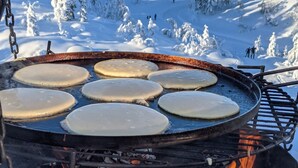 A circular grill with pancakes cooking over an open flame, set against a snowy mountain backdrop. - Fantastic and large cottage on top of Furuåsen in the heart of Sirdal (Tjørhom)