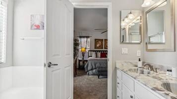 A modern bathroom with a large mirror, a bathtub, and a vanity with a marble countertop.