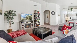A modern living room with a fireplace, a television, and a dining area with a kitchen in the background. - Beautiful n Cozy - Great Location - Private Heated Pool (Chandler)